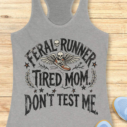 Gray tank top with 'Feral Runner Tired Mom Don't Test Me' text and graphic on a wooden surface.