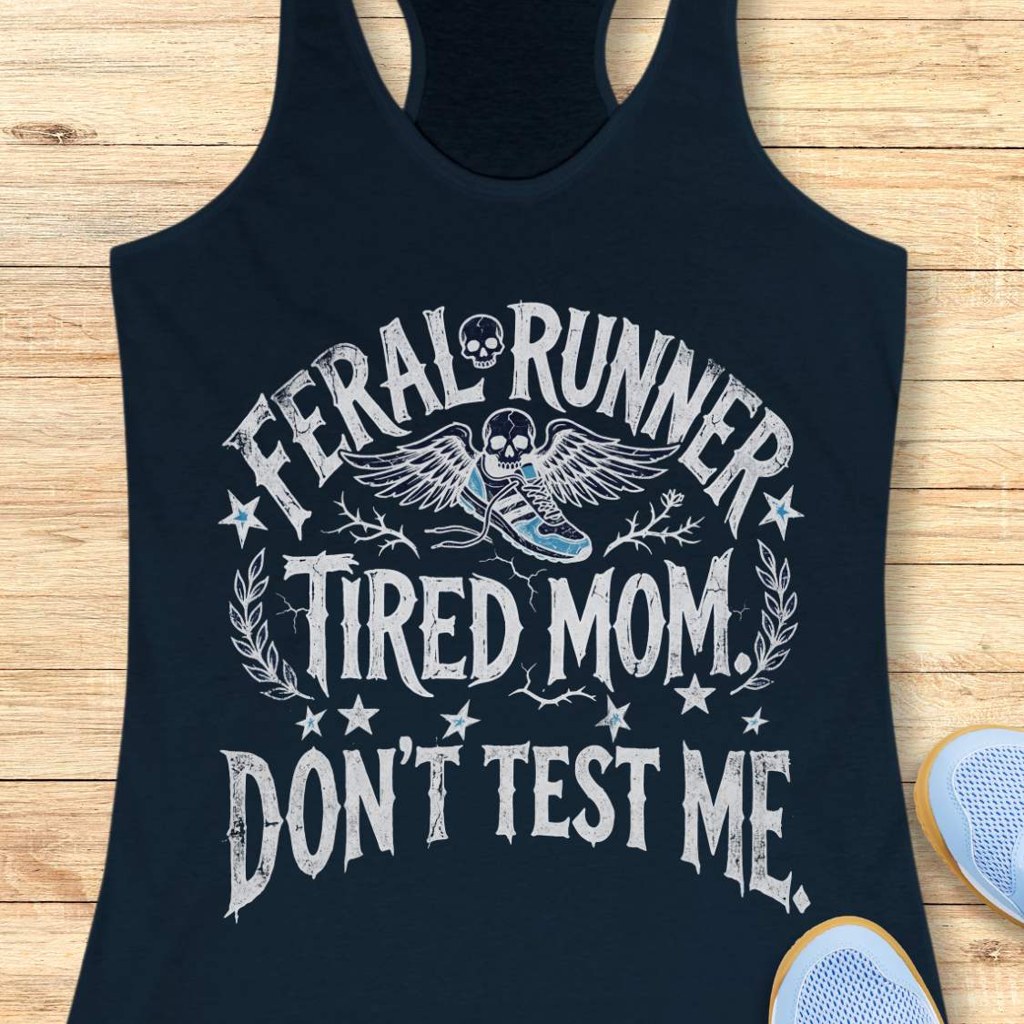 navy tank top with white text 'feral runner, tired mom. Don't test me.',  and graphics on a wooden surface