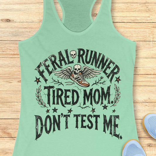 Mint green tank top with text 'feral runner, tired mom. Don't test me.', and graphic design on a wooden surface