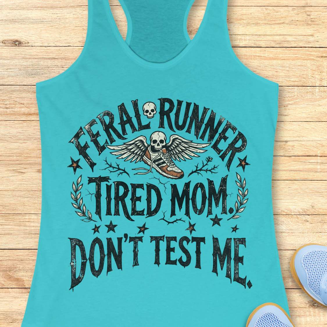 Turquoise tank top with text 'Feral Runner Tired Mom Don't Test Me' on a wooden surface.