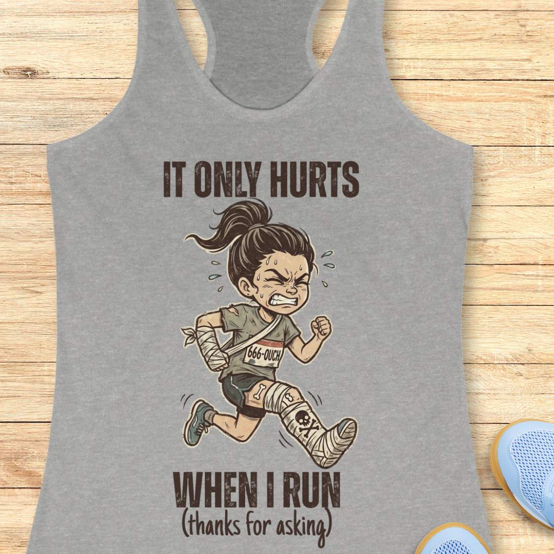 Gray tank top with cartoon character and text 'It only hurts when I run (thanks for asking)', on a wooden surface