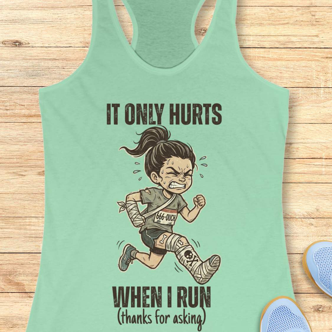 Light green tank top with a graphic of a runner and text 'It only hurts when I run (thanks for asking)', on a wooden surface