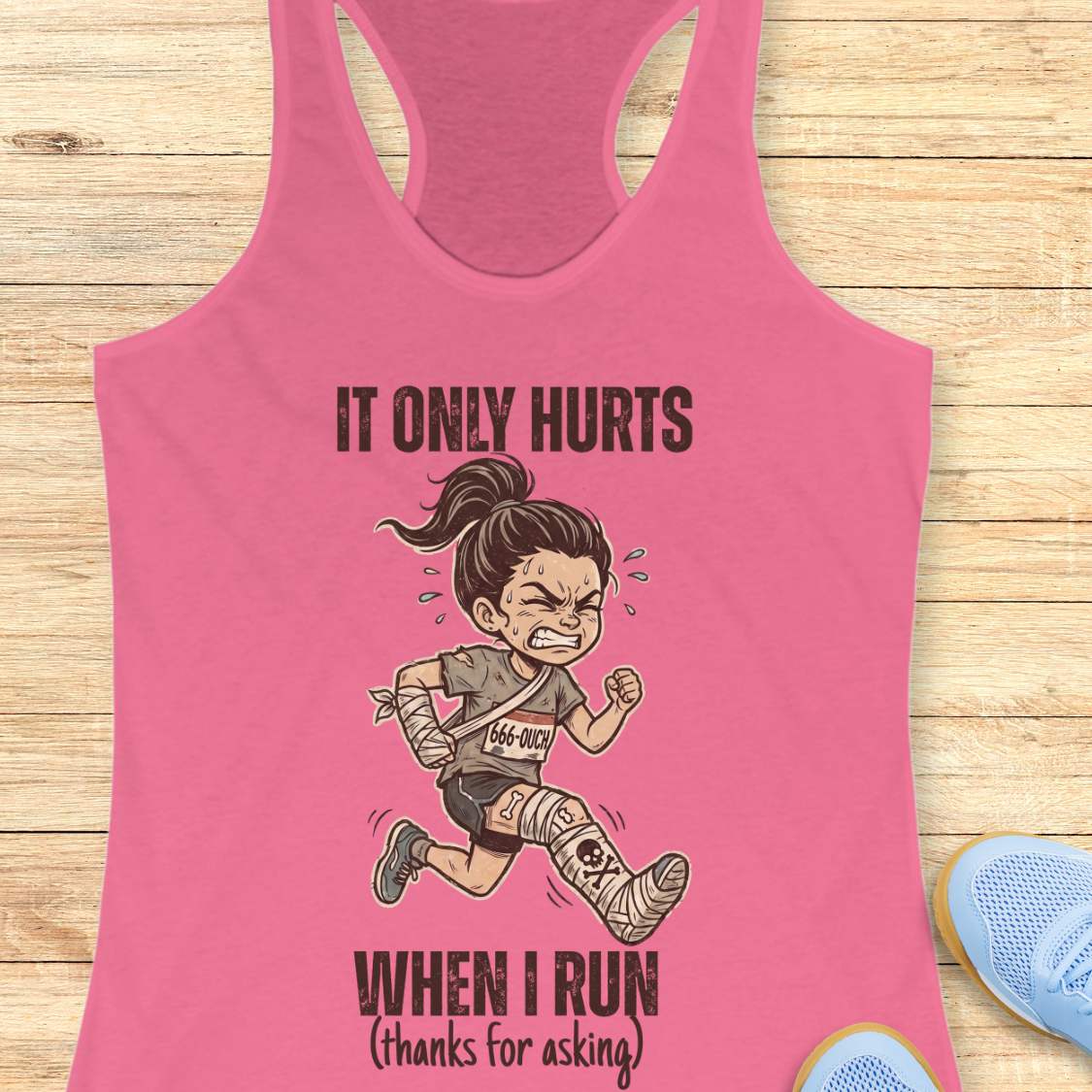 Pink tank top with cartoon character and text 'It only hurts when I run (thanks for asking)', on a wooden surface
