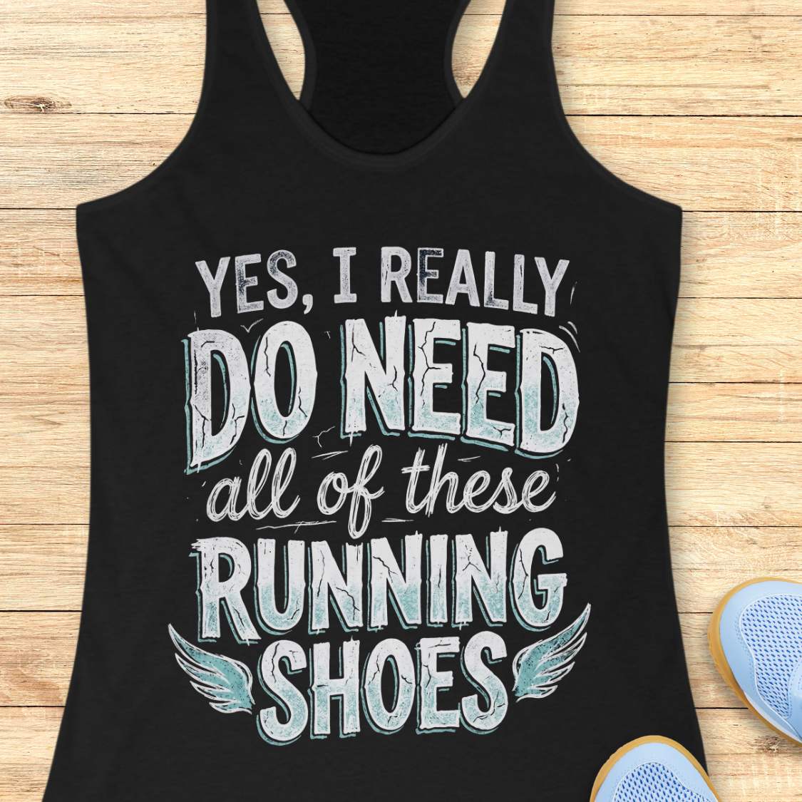 Black tank top with motivational text ' yes, I really do need all of these running shoes', on a wooden surface