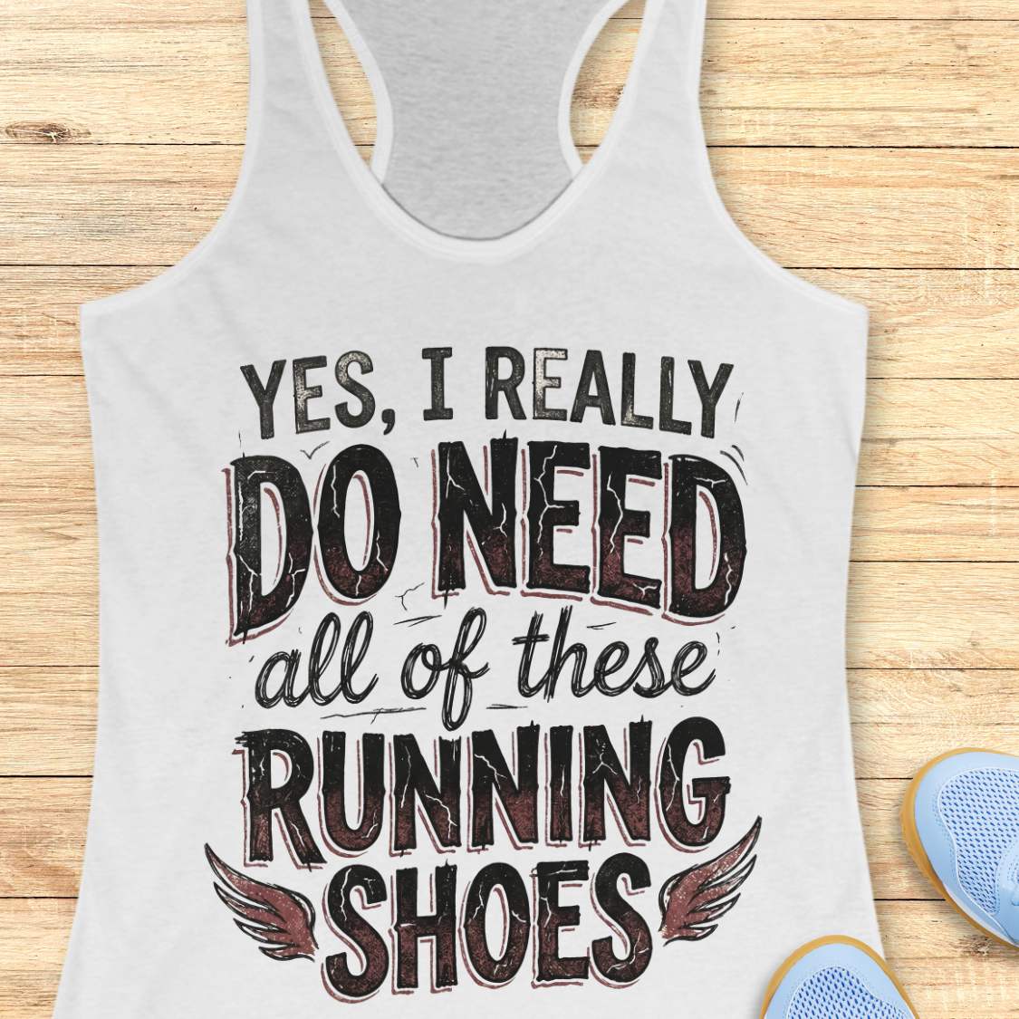 white tank top with text 'Yes, I really do need all of these running shoes' on a wooden surface.