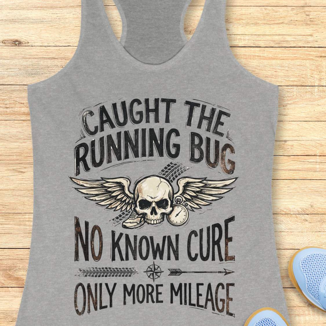 Gray tank top with skull and text 'caught the running bug. no known cure. only more mileage', design on a wooden surface
