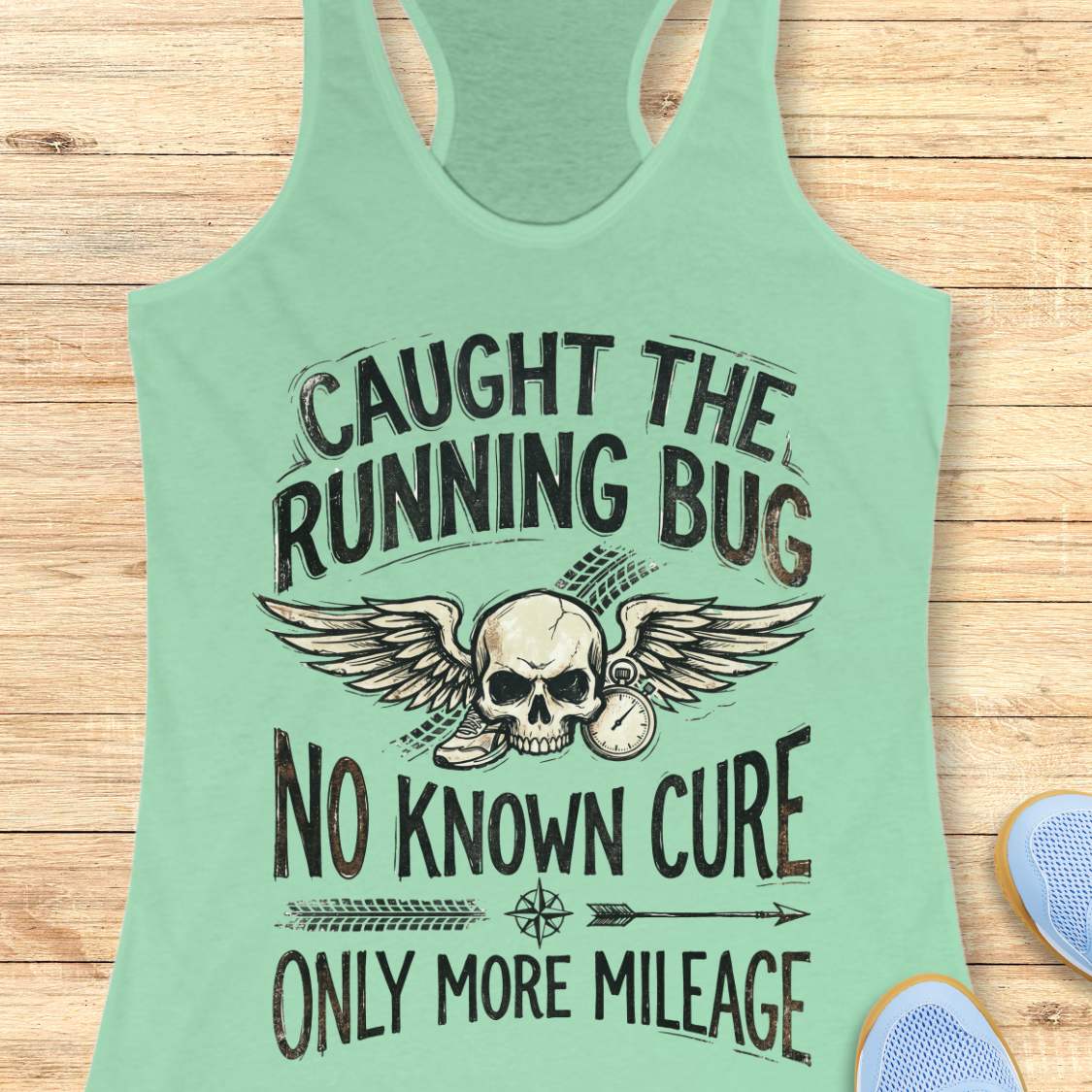 Mint green tank top with skull and text 'caught the running bug. no known cure. only more mileage', design on a wooden surface
