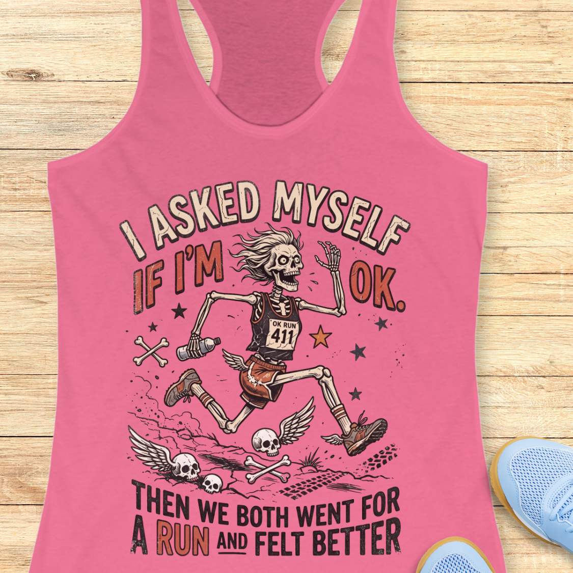 Pink tank top with skeleton design and text 'I asked myself if I'm OK. Then we both went for a run and felt better',  on a wooden surface