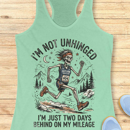 Mint green tank top with skeleton graphic and text 'I'm not unhinged, I'm just two days behind on my mileage', on a wooden surface
