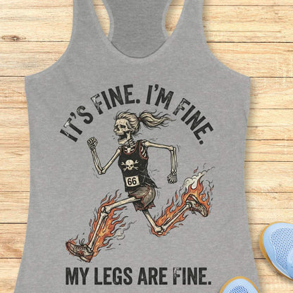 Gray tank top with skeleton design and text 'It's fine. I'm fine. My legs are fine.', on a wooden surface