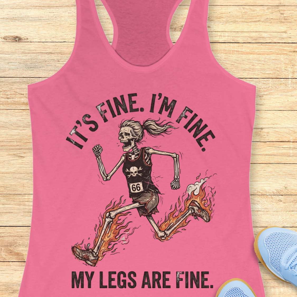 Pink tank top with skeleton runner graphic and text  'It's fine. I'm fine. My legs are fine.',  on a wooden surface
