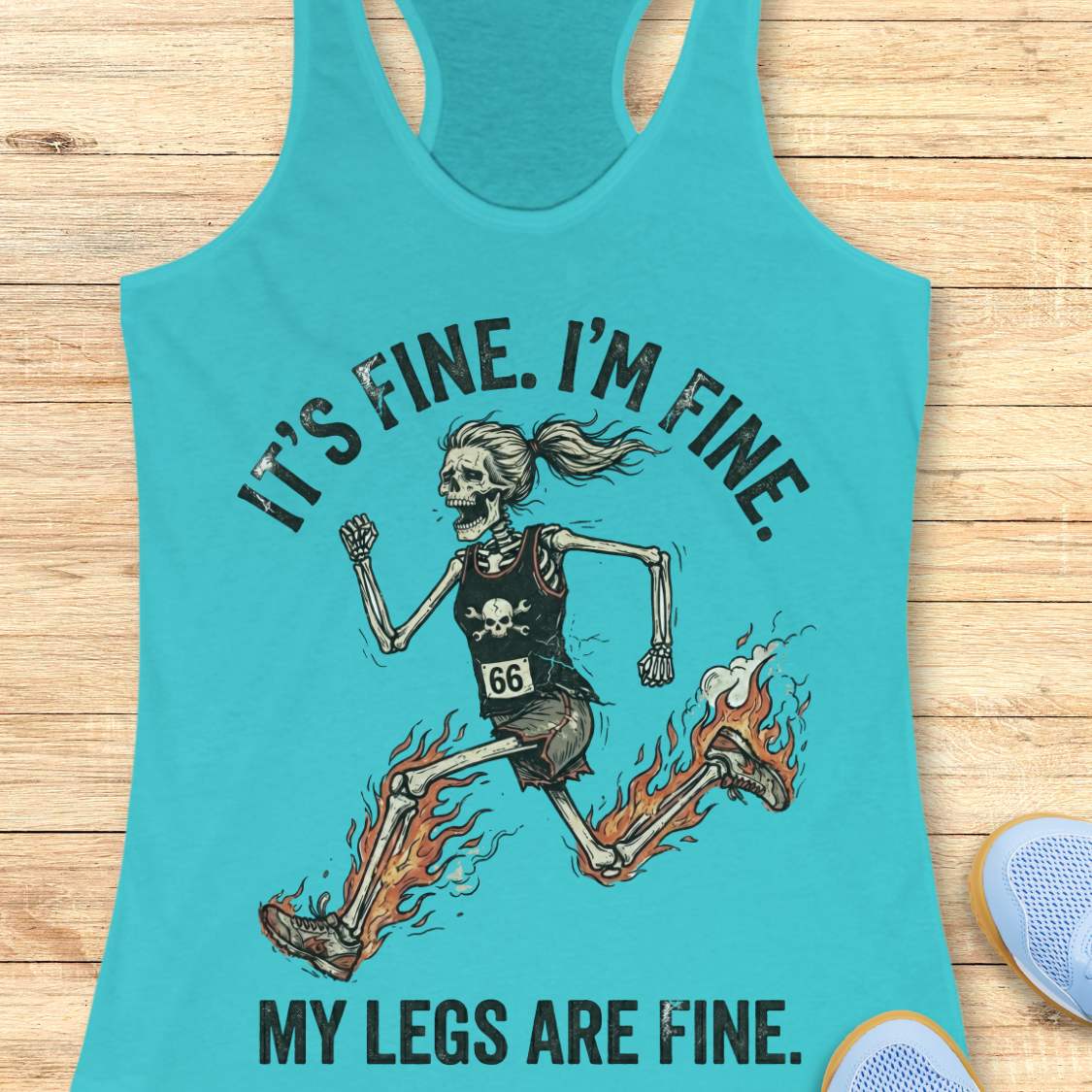 Turquoise tank top with skeleton design and text  'It's fine. I'm fine. My legs are fine.',  on a wooden surface