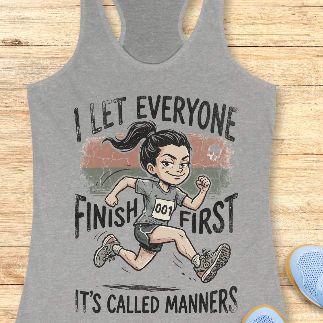 Gray tank top with a graphic of a runner and text  'I let everyone finish first. It's called manners', on a wooden surface
