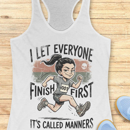 white tank top with a graphic of a runner and text 'I let everyone finish first. It's called manners', on a wooden surface