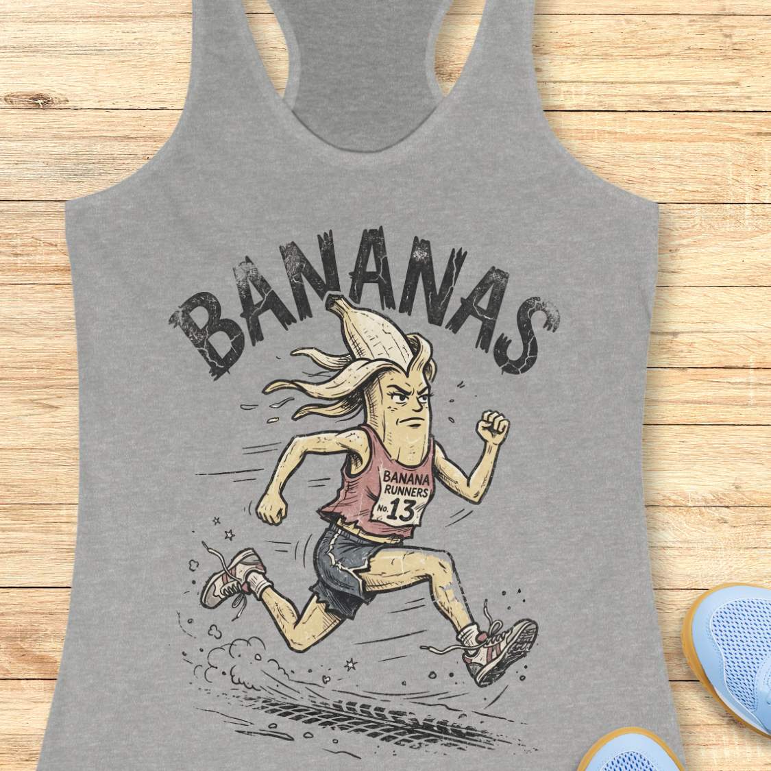 Gray tank top with cartoon banana character and 'BANANAS' text on a wooden surface