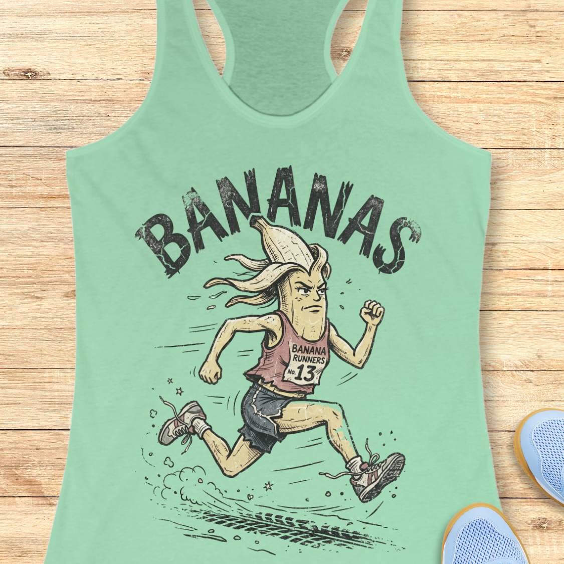 Mint green tank top with a cartoon banana character and 'BANANAS' text on a wooden surface.