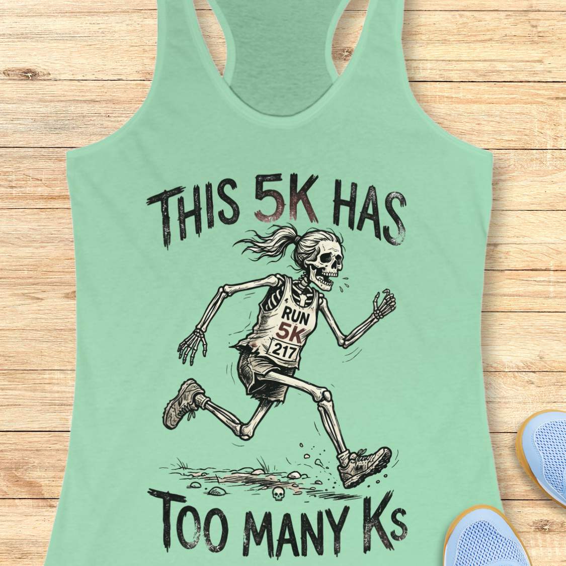 Mint tank top with skeleton running design and text 'This 5k has too many Ks',  on a wooden surface