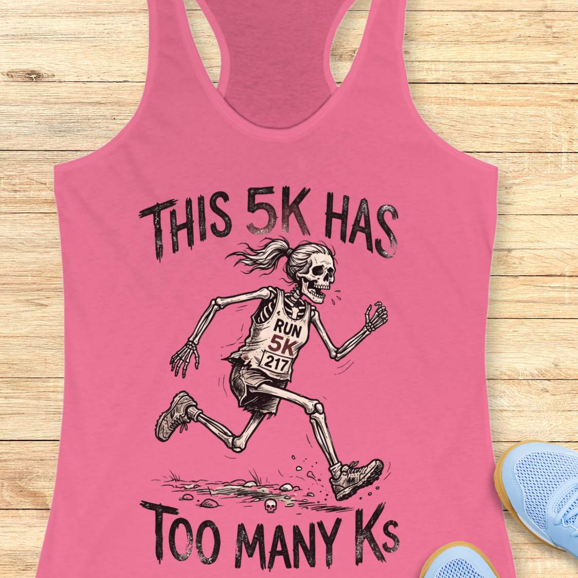 Pink tank top with skeleton running design and text 'This 5k has too many Ks',  on a wooden surface