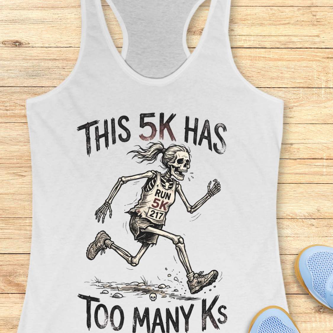 white tank top with skeleton running design and text 'This 5k has too many Ks',  on a wooden surface