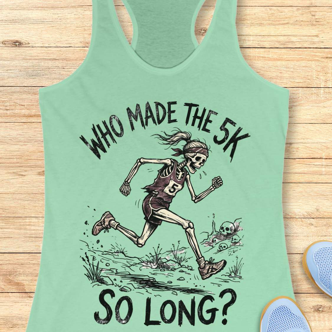 Light green tank top with skeleton running graphic and text 'WHO MADE THE 5K SO LONG?' on a wooden surface.