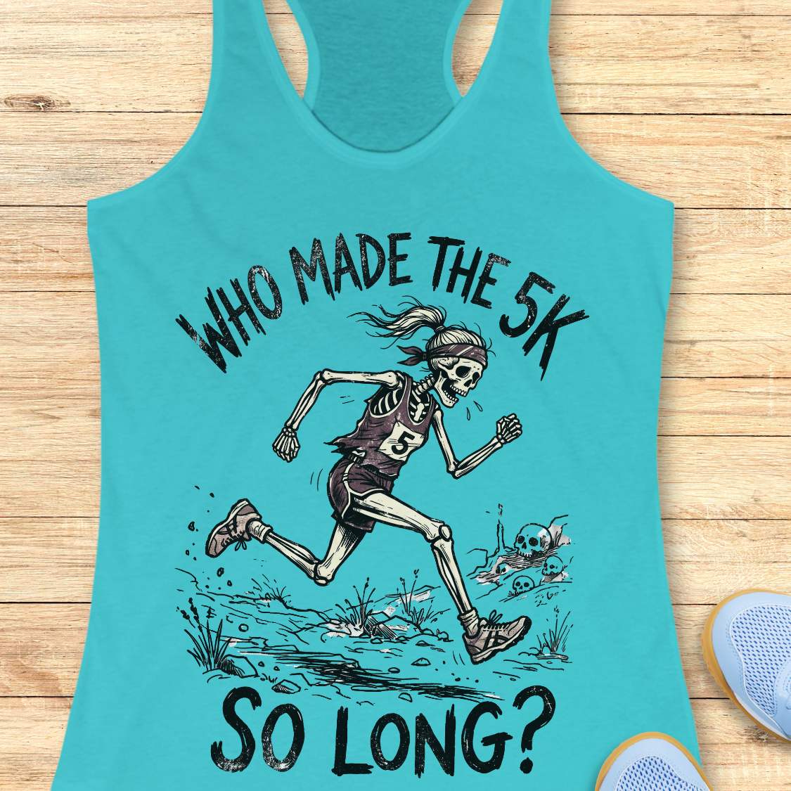 Turquoise tank top with skeleton running graphic and text 'WHO MADE THE 5K SO LONG?' on a wooden surface.
