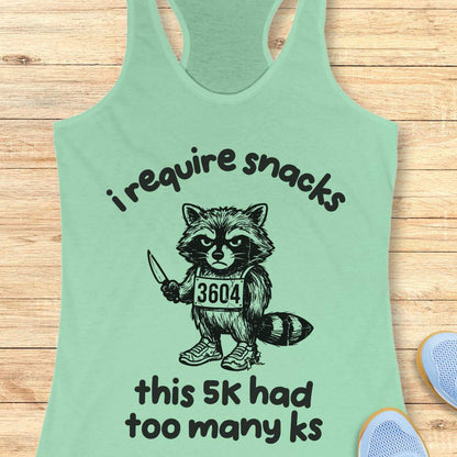Mint green tank top with a graphic of a raccoon and text 'i require snacks, this 5k had too many ks', on a wooden surface