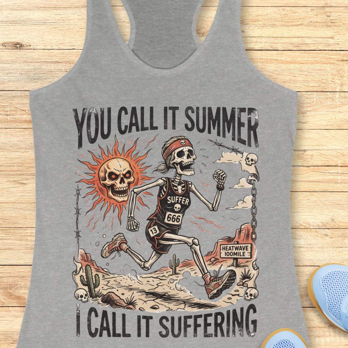 Gray tank top with skeleton graphic and text 'you call it summer, I call it suffering',  on a wooden surface