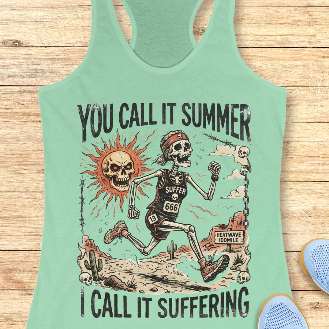Mint green tank top with skeleton graphic and text 'you call it summer, I call it suffering',  on a wooden surface