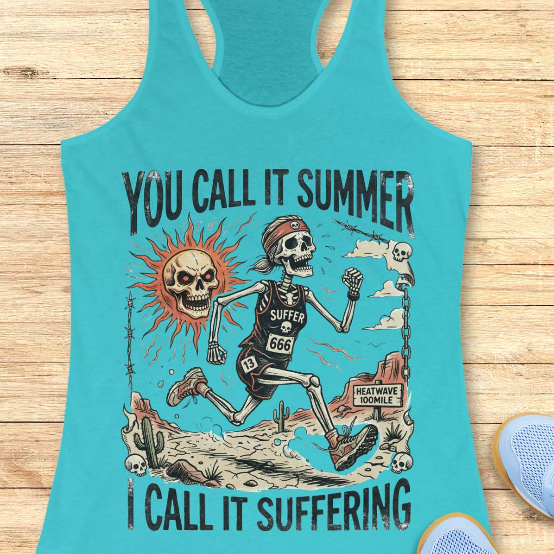 Turquoise tank top with skeleton graphic and text 'you call it summer, I call it suffering', on a wooden surface