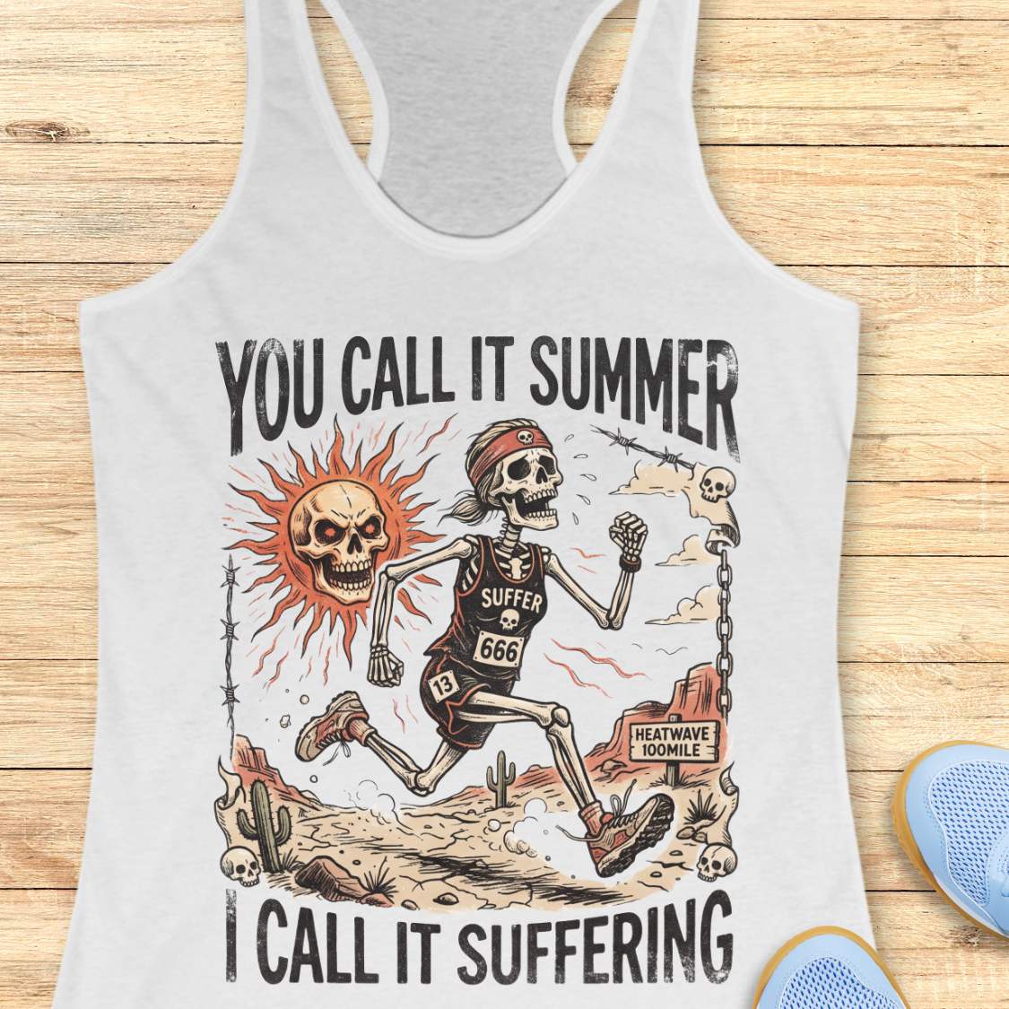 white Tank top with skeleton graphic and text 'you call it summer, I call it suffering', on a wooden surface