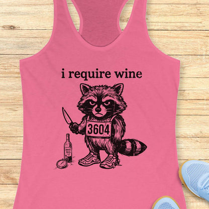 Pink tank top with a raccoon graphic and text 'i require wine' on a wooden surface.