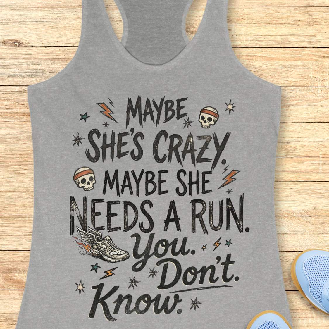 grey tank top with black graphic design and text 'maybe she's crazy, maybe she needs a run. you. don't. know.', on a wooden surface