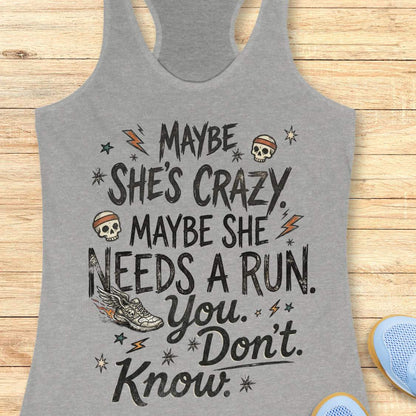 grey tank top with black graphic design and text 'maybe she's crazy, maybe she needs a run. you. don't. know.', on a wooden surface