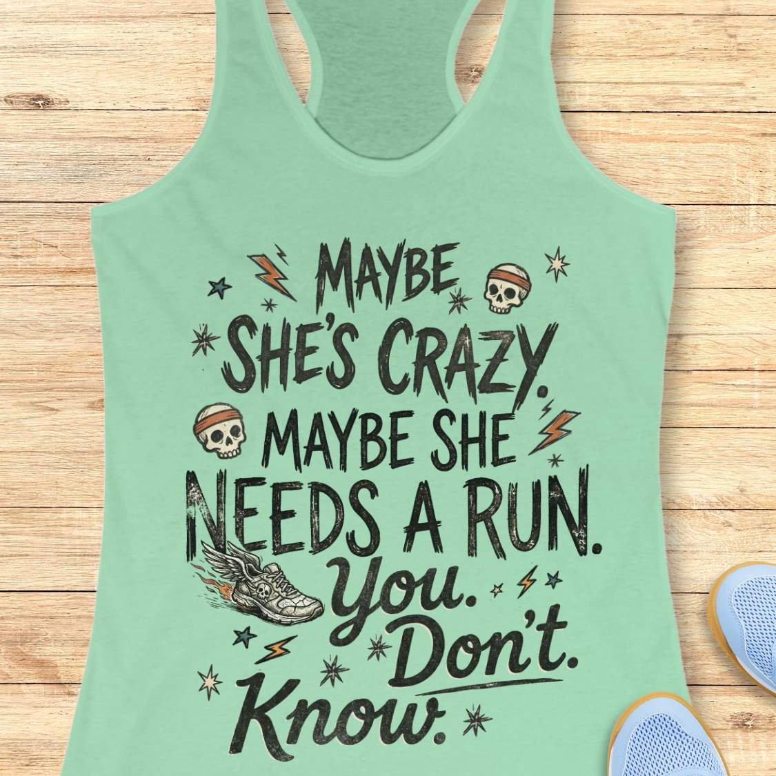 mint tank top with black graphic design and text 'maybe she's crazy, maybe she needs a run. you. don't. know.', on a wooden surface
