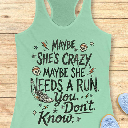 mint tank top with black graphic design and text 'maybe she's crazy, maybe she needs a run. you. don't. know.', on a wooden surface
