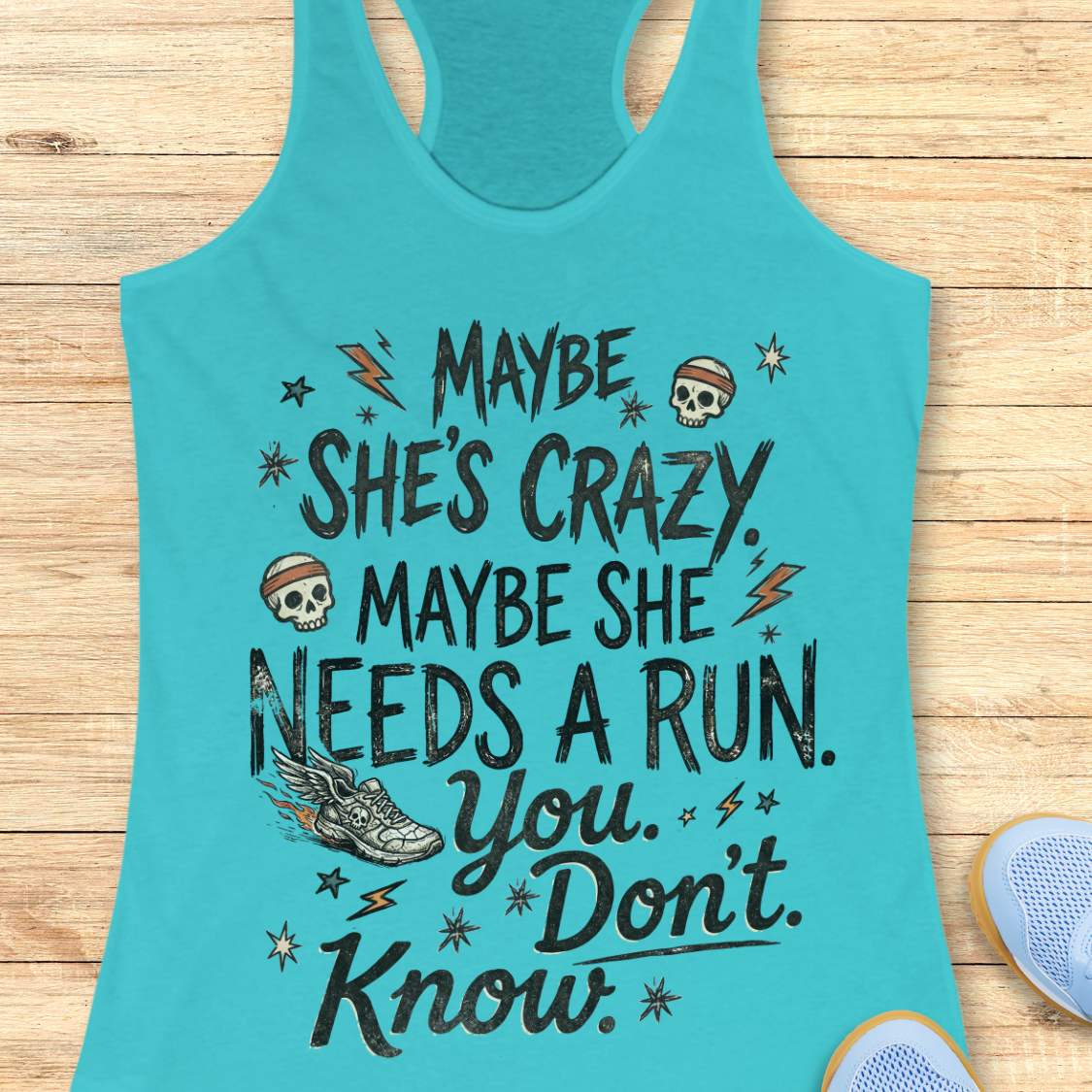 tahiti blue tank top with black graphic design and text 'maybe she's crazy, maybe she needs a run. you. don't. know.', on a wooden surface