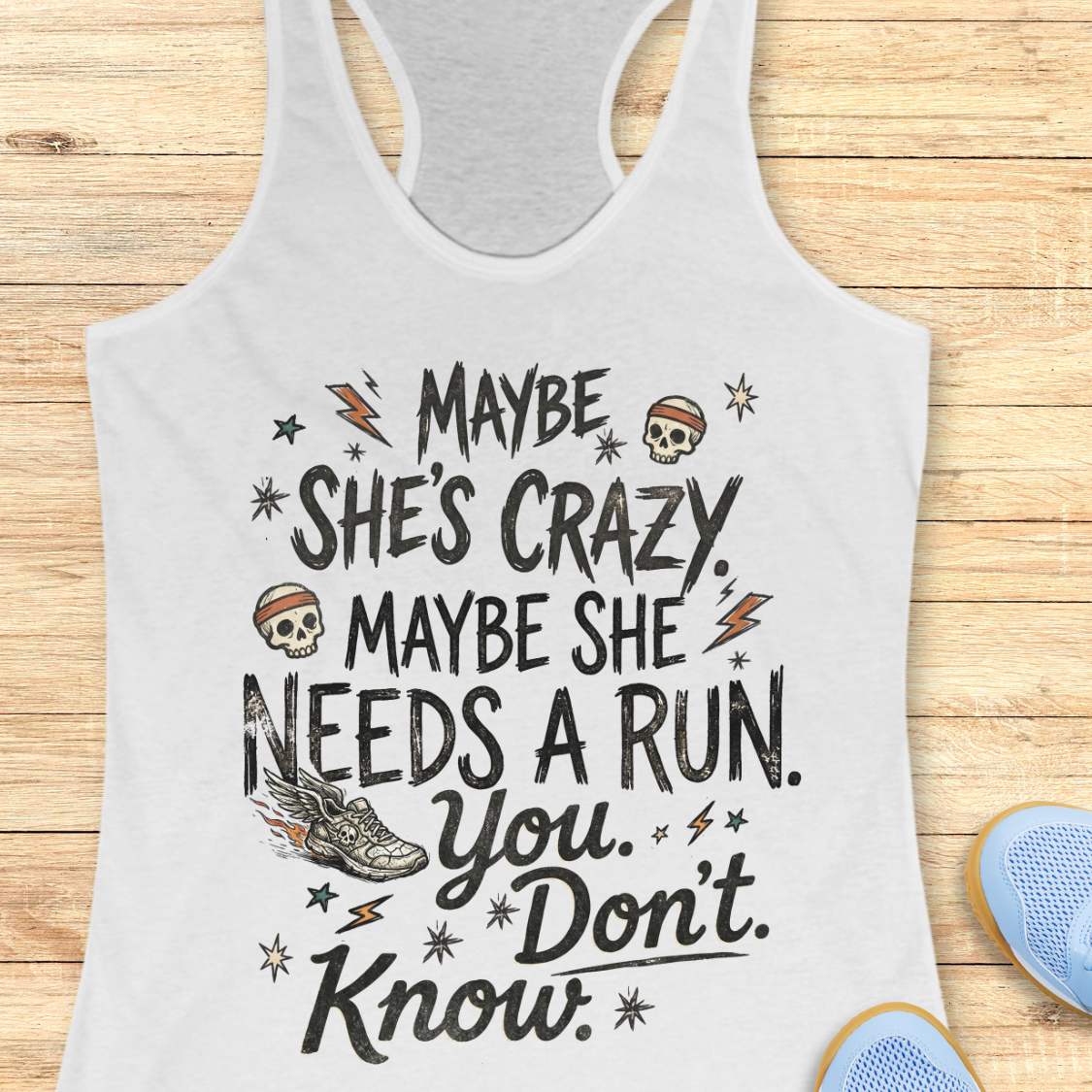 white tank top with black graphic design and text 'maybe she's crazy, maybe she needs a run. you. don't. know.', on a wooden surface
