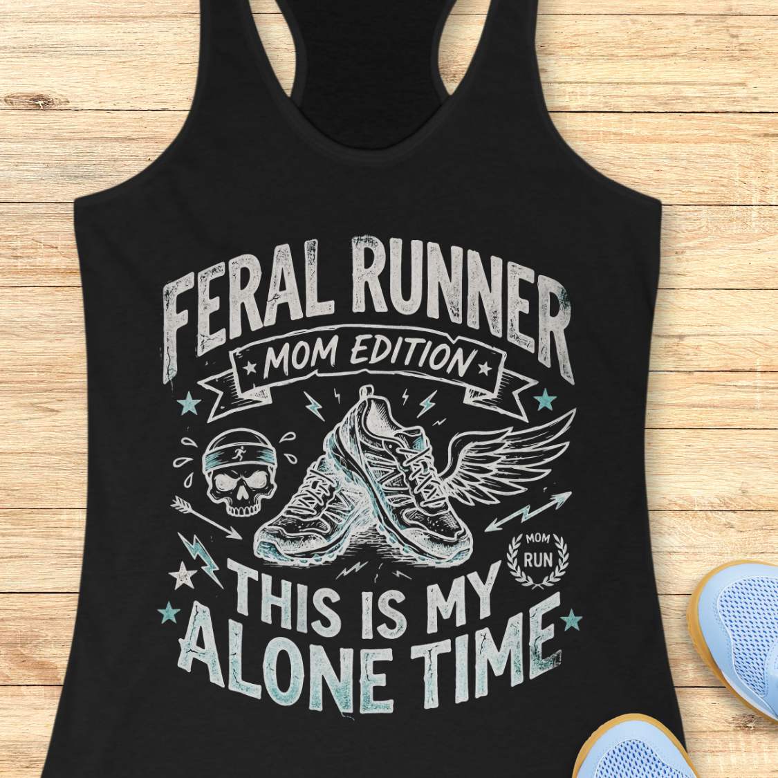black tank top with black graphic design and text 'feral runner, mom edition. This is my alone time', on a wooden surface