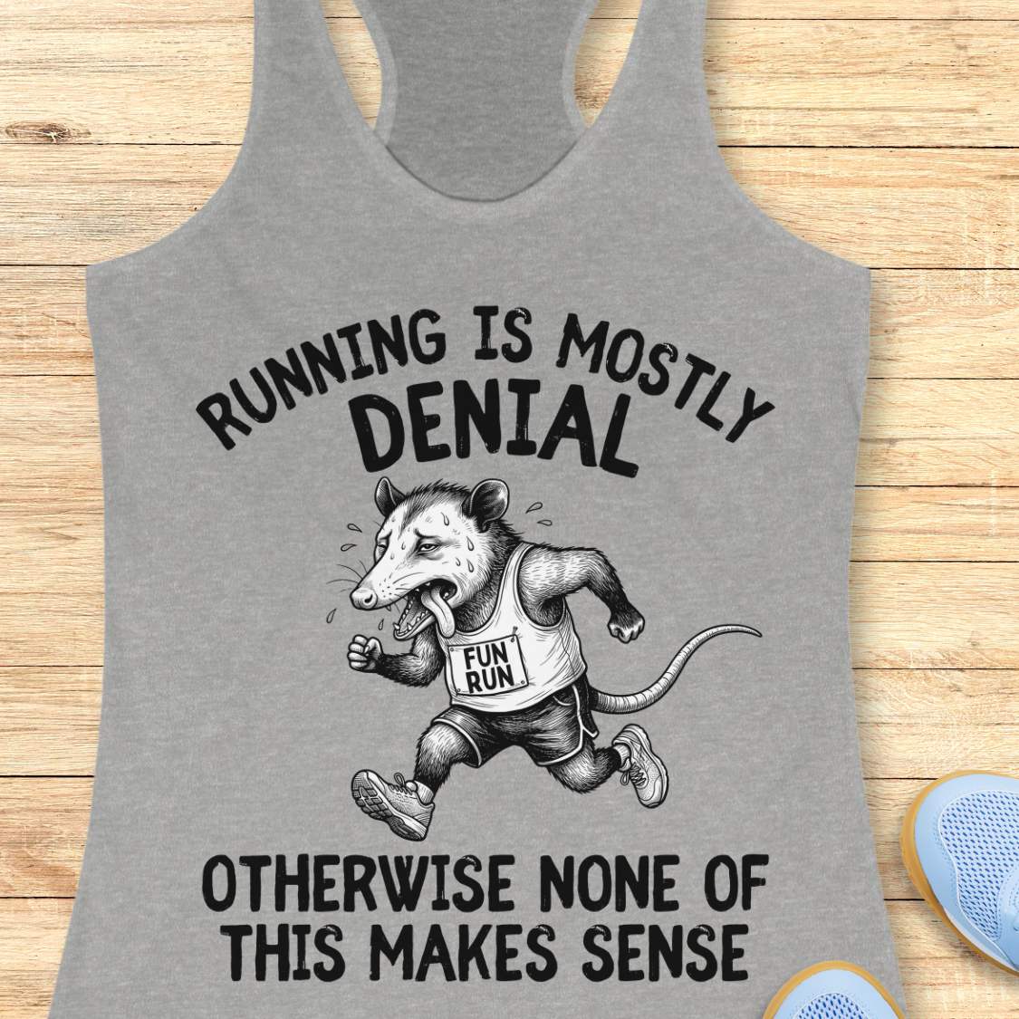 grey tank top with black graphic design and text 'running is mostly denial. otherwise, none of this makes sense.', on a wooden surface