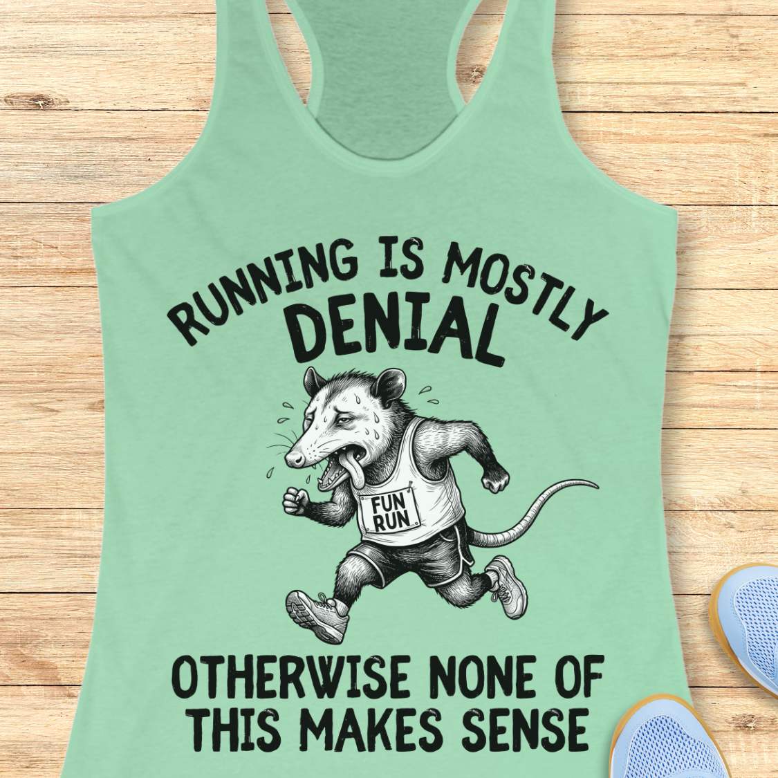 mint tank top with black graphic design and text 'running is mostly denial. otherwise, none of this makes sense.', on a wooden surface