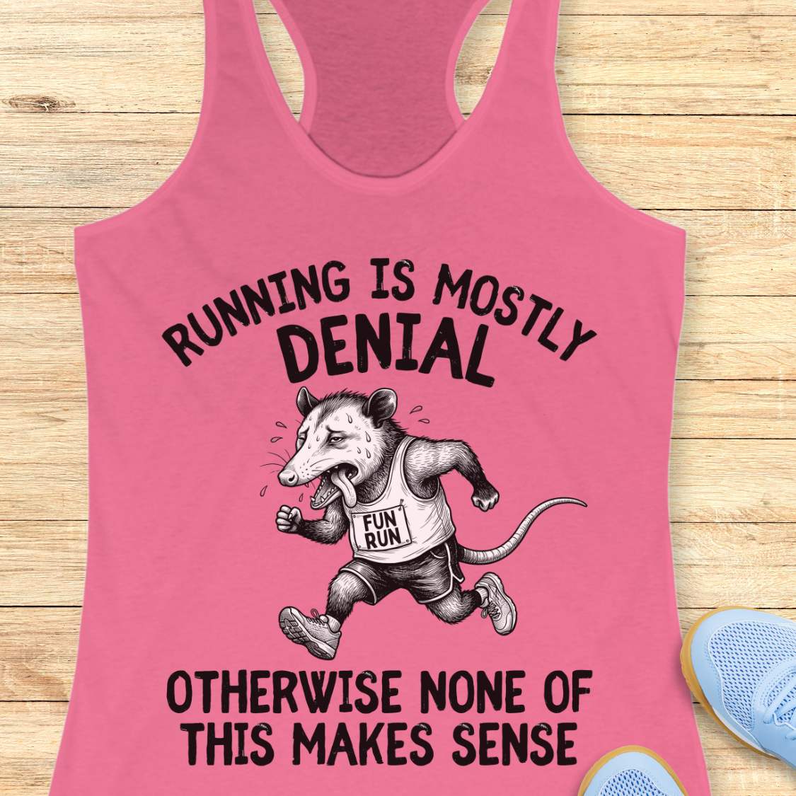 pink tank top with black graphic design and text 'running is mostly denial. otherwise, none of this makes sense.', on a wooden surface