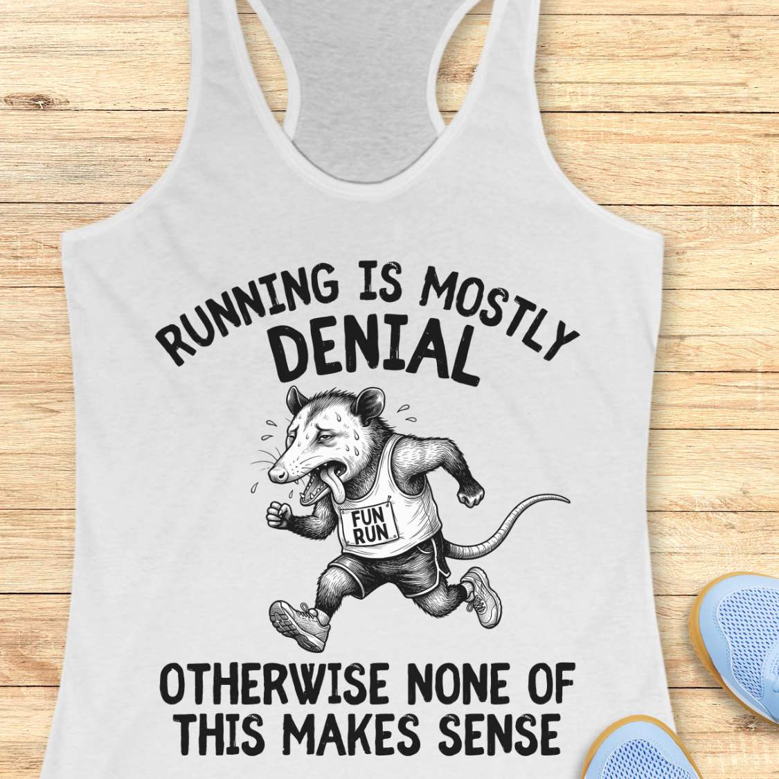 white tank top with black graphic design and text 'running is mostly denial. otherwise, none of this makes sense.', on a wooden surface