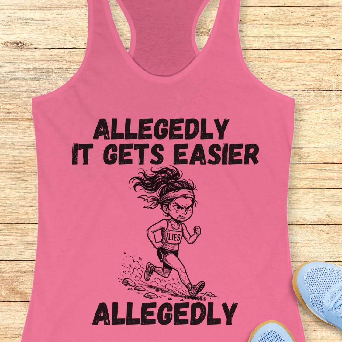 pink tank top with black graphic design and text 'allegedly it gets easier. Allegedly.', on a wooden surface