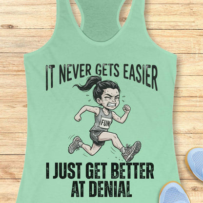 mint tank top with black graphic design and text 'it never gets easier, I just get better at denial', on a wooden surface