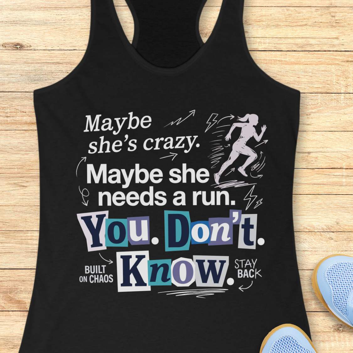 black tank top with graphic design and text 'Maybe she's crazy. Maybe she needs a run. You. Don't. Know.', on a wooden surface
