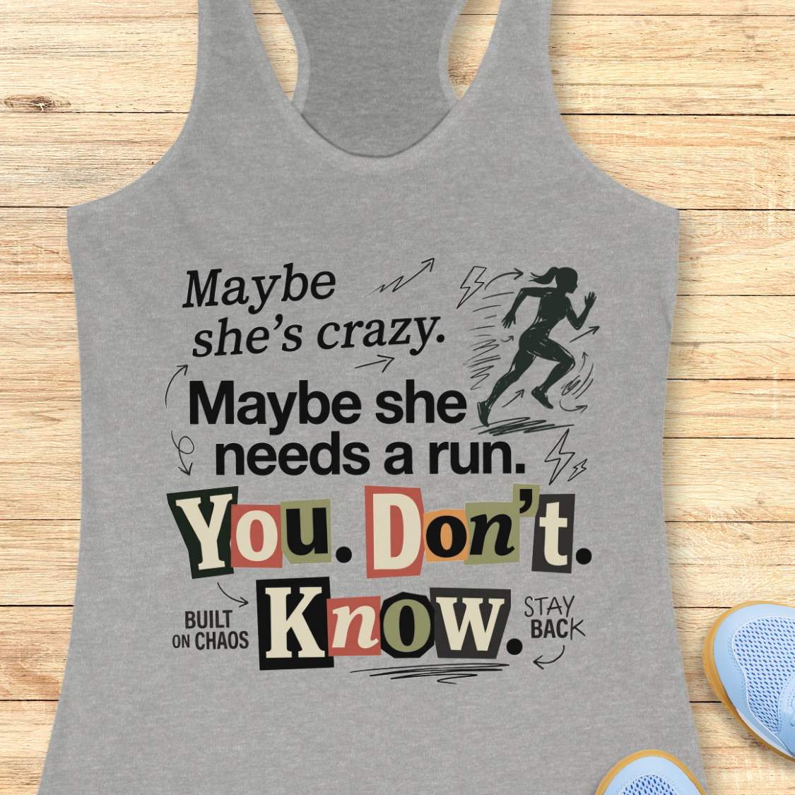 grey tank top with graphic design and text 'Maybe she's crazy. Maybe she needs a run. You. Don't. Know.', on a wooden surface