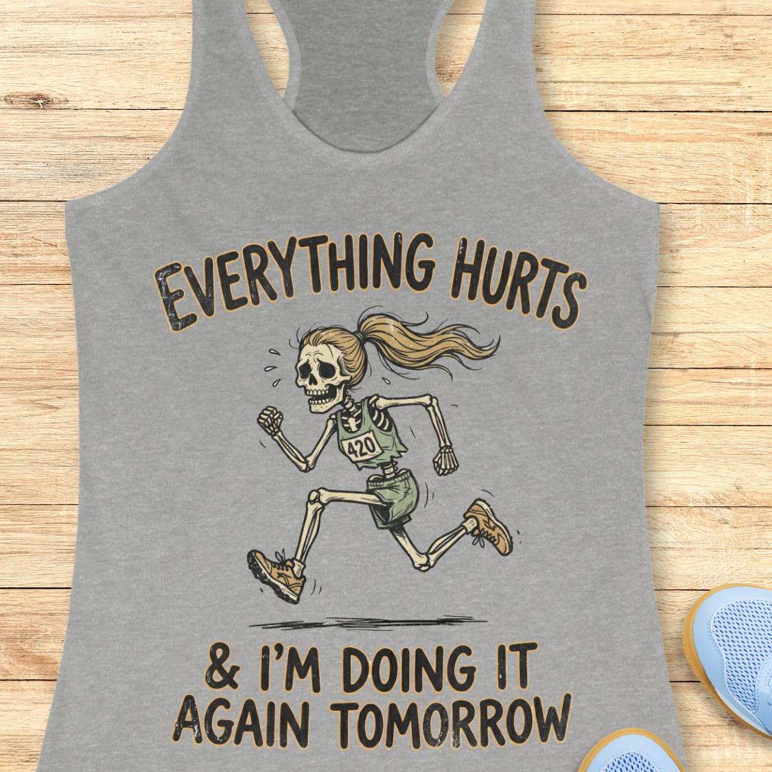grey tank top with graphic design of a runner skeleton and text 'Everything hurts and I'm doing it again tomorrow', on a wooden surface