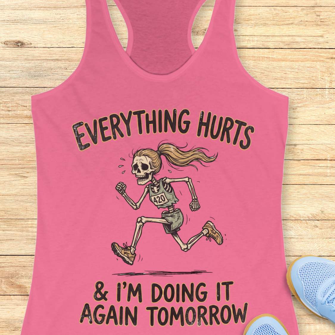 pink tank top with graphic design of a runner skeleton and text 'Everything hurts and I'm doing it again tomorrow', on a wooden surface
