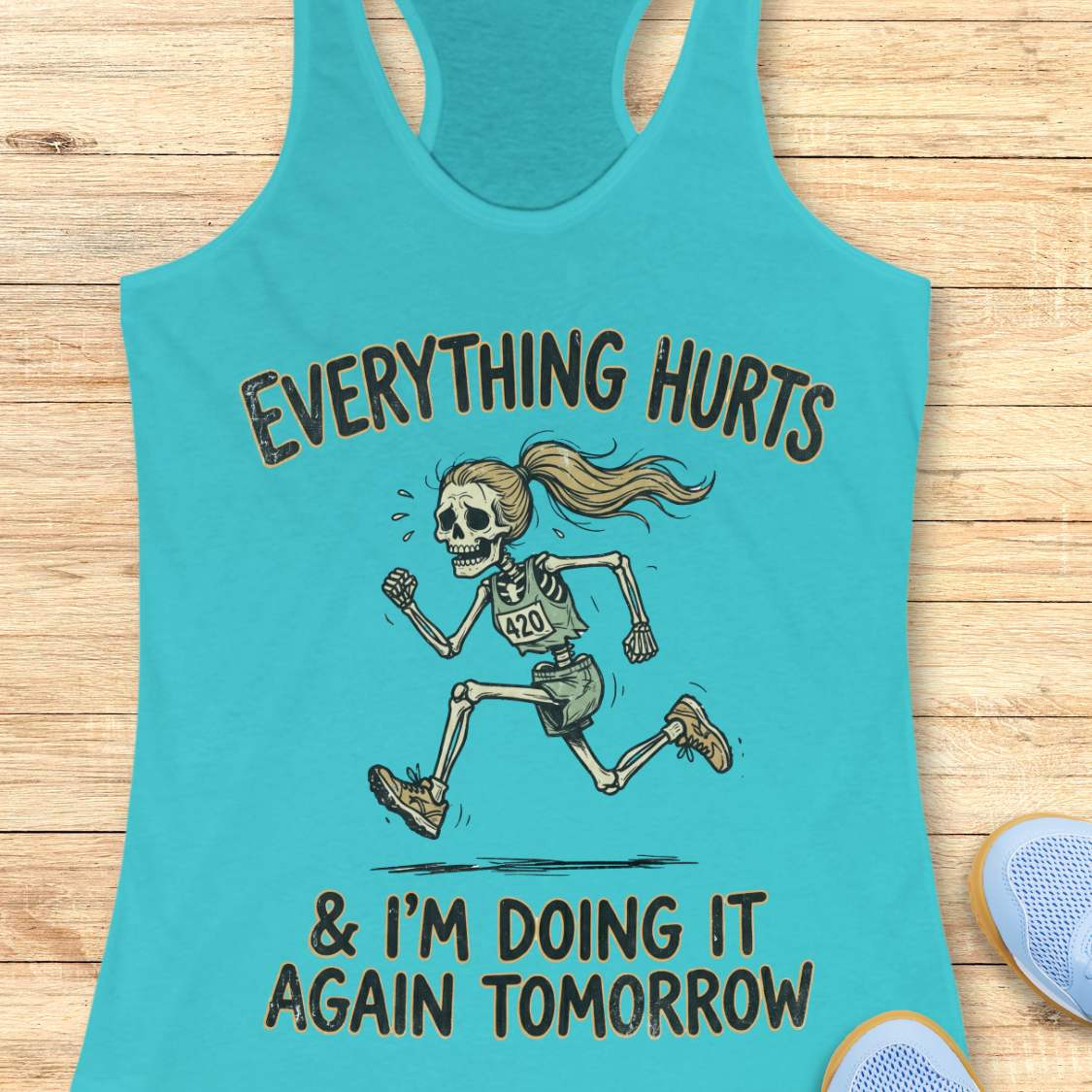 blue tank top with graphic design of a runner skeleton and text 'Everything hurts and I'm doing it again tomorrow', on a wooden surface