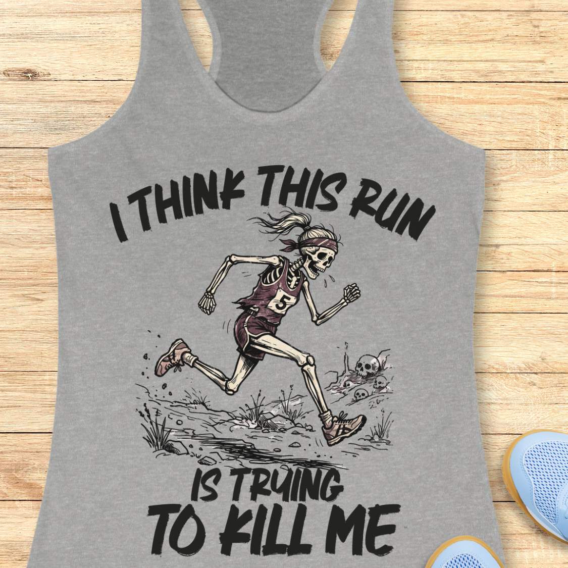 grey tank top with graphic design of a runner skeleton and text 'I think this run is trying to kill me', on a wooden surface